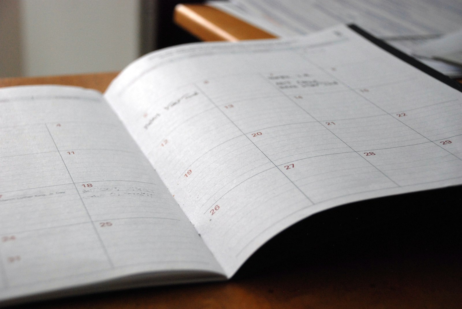 An open monthly planner on a wooden desk, the month laid out as a grid of empty squares.
