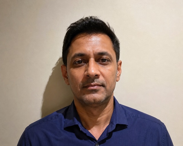 A portrait taken in a cluttered room with shelves and objects visible behind the subject